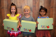 three children are standing in front of a wooden wall. they are each holding a wiggle worms kit box..