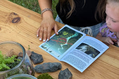 A mom and daughter reading the story in the paperwork with a terrarium and some hardscape components in the foreground.