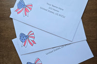 Three white envelopes with printed sample U.S. mailing addresses and red, white and blue patriotic bow designs featuring stars and stripes.