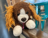 The front of Snorri hanging out on the edge of a chair while out and about in the world. This shows that the stuffed animal can travel. 