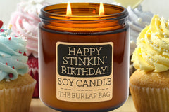 Happy Stinkin' Birthday 16oz double-wick soy candle by The Burlap Bag, cupcake scented amber jar beside frosted birthday cupcakes