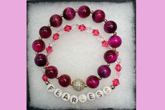 Handmade encouragement bracelet with soft pink stone beads, rose faux crystal accents, and white letter beads spelling “FEARLESS” 