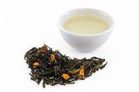 Lulada green tea from Colombia's Bitaco garden, twisted leaves with pieces of lulo fruit, beside a white cup of pale gold tea