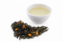 Lulada green tea from Colombia's Bitaco garden, twisted leaves with pieces of lulo fruit, beside a white cup of pale gold tea