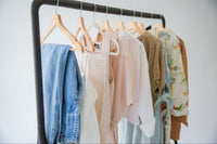 a rack of vintage garments for spring, floral print wraps, cotton blouses and denim jeans, all perfect layering pieces for the season
