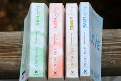 Set of four books from Ana Huang with colors green, pink, yellow and blue. They are all laying on a wooden bench.