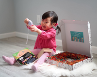 Smiling toddler opening Owl Post Books kids subscription box with books and crafts, a perfect holiday gift for young readers.