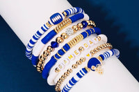Close-up of a wrist wearing the Game Day 8-piece stackable friendship bracelet set in blue and white beads with gold accents, football charm