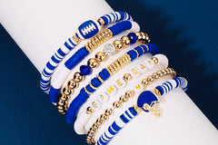 Close-up of a wrist wearing the Game Day 8-piece stackable friendship bracelet set in blue and white beads with gold accents, football charm