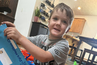 A boy sitting on the floor pulls his personalized letter out of a blue Zip's Mailbox Club envelope, smiling as he opens his mail.