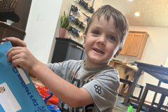 A boy sitting on the floor pulls his personalized letter out of a blue Zip's Mailbox Club envelope, smiling as he opens his mail.
