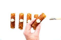 Apple Pie Brandy Snaps DIY baking kit result with 28 filled lace desserts arranged in four neat rows on a white tray.