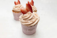Bright lemon cupcakes topped with pink strawberry buttercream swirls and white sugar pearls in a baking kit setup