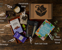 Introverts Retreat flatlay on wood with each item and the box. Items are labeled with white lettering.