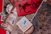 Scarlet Envelope Secret Society subscription box featuring a red envelope and various mystery-themed materials for puzzles