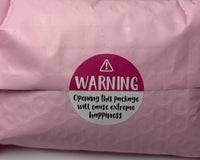 Pink bubble mailer packaging with a warning label sticker that reads opening this package will cause extreme happiness, shown as part of pro