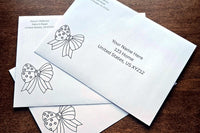Three white envelopes with printed sample U.S. mailing addresses and black outline patriotic bow designs arranged on a wooden table.