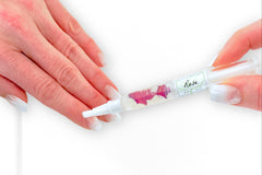 A Greenmade goods Rose Cuticle Oil held in the right hand, applying to the left against a light background.