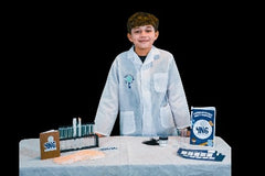 A child in a lab coat is standing at a table. On the table various items are displayed, including test tubes, and fingerprint cards. 