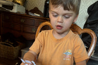 A boy at the dining table opens his Zip's Mailbox Club mail and looks through the stamps and pages that came inside the red envelope.