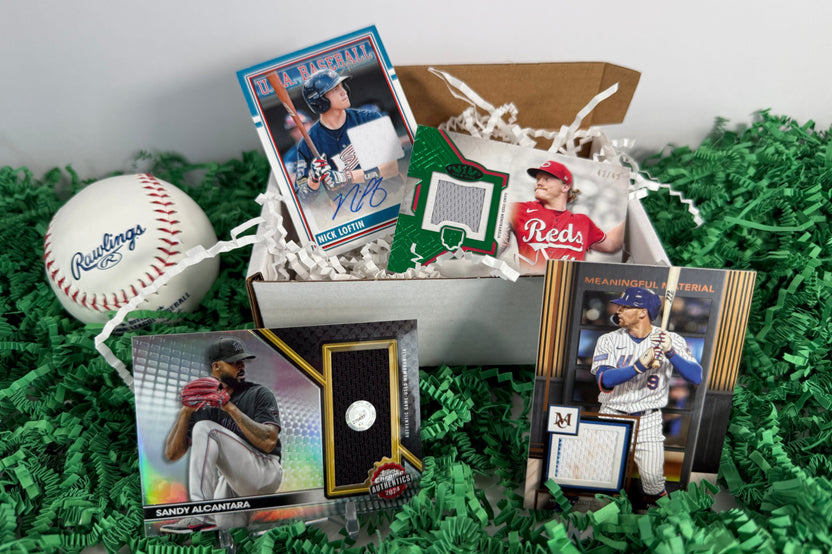 Four autographed and game-used baseball cards in a box, with a baseball, placed on a green grass mat