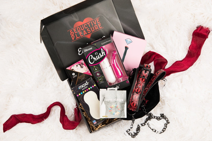 Black box tied with a red ribbon next to dessert and drinks for the Ultimate Adult Boxes For Couples subscription