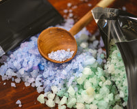Introverts Retreat box closeup of blue and green bath salts spilling out of black bags with a wooden scoop.