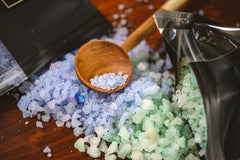 Introverts Retreat box closeup of blue and green bath salts spilling out of black bags with a wooden scoop.