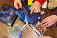 Photo of 3 peoples hands holding pieces of papers that contain information to a escape mystery game puzzle.