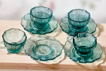This is a photograph of a tiny miniature set of greenish blue dishes.   It is a teacup and saucer.  They are very small.