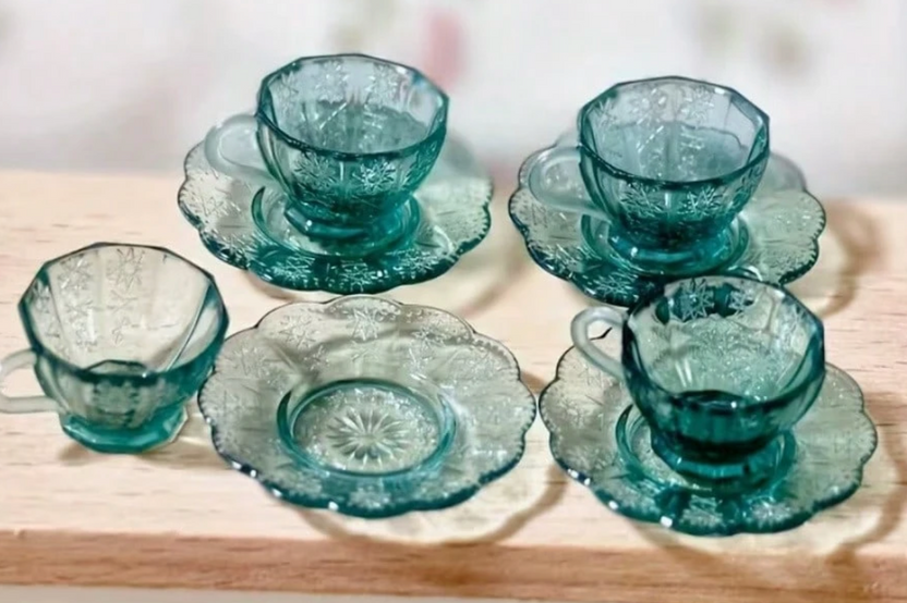 This is a photograph of a tiny miniature set of greenish blue dishes.   It is a teacup and saucer.  They are very small.