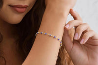 Close-up of the evil eye bracelet worn on a wrist, featuring small blue evil eye charms spaced along a 14K gold plated gold-tone chain.