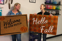 Two women showing off there hand painted fall door mats | Panache Craft Box - Monthly Craft Box + Live Virtual Art Class 
