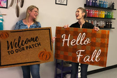Two women showing off there hand painted fall door mats | Panache Craft Box - Monthly Craft Box + Live Virtual Art Class 
