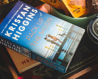 Introverts Retreat Read Box contents: A book called Pack Up the Moon with treats on a wooden background.