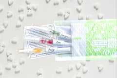 Greenmade goods Lemongrass, Rose, and Orange cuticle oils in a green and white envelope against a white background surrounded by hearts.
