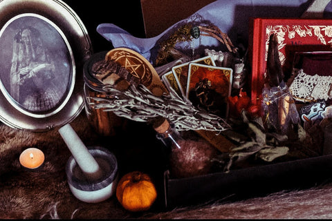 black box with dried herbs, a book, socks, tarot cards, a wreath, and potions inside. decorated with candles and an eerie photo