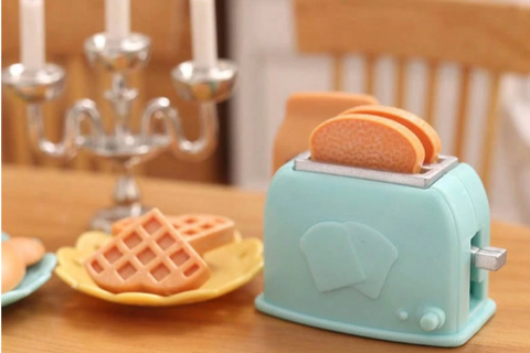 This is a photograph of a tiny blue miniature toaster oven with toast popping out the top.  There are two waffles on a plate.