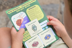 Child holding Bug Badges “Garden Snail” Discovery Hints card with three collectible enamel pins - monthly subscription box for kids.