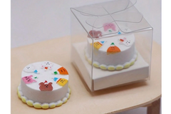 This is a photograph of a tiny miniature birthday cake in a clear deli box.  There are bears on the cake.