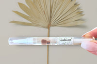 Hand Holding The Sandalwood Cuticle Oil Pen by Greenmade goods With a Dried Palm Sprig in the Background.