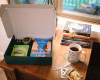 Books & More book box with two great reads and novelty items- a tin candle, eye masks, earrings, etc. Indulge in self care and relaxation.