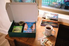 Box of Books subscription box featuring "An Academic Affair," a candle, tea, and a cozy mug for relaxation