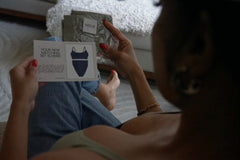 A woman sitting down holding her packaged items from Noux in one hand and reading her notecard in the other hand