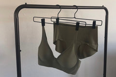 Green seamless bra and green pair of seamless briefs hanging each hanging from an industrial clothing rack