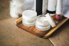 Skin care and body care products placed on a wooden tray that is on a wooden table. There is almost no background.