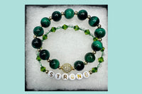 Handmade encouragement bracelet with rich green stone beads, clear and green faux crystal accents, and white letter beads spelling “STRONG” 