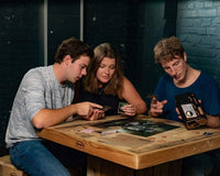 three people sitting at a table and playing a mystery escape game with thrilling story. There are 2 men and one woman.