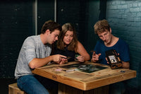 three people sitting at a table and playing a mystery escape game with thrilling story. There are 2 men and one woman.