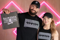 This image shows a husband and wife couple, where the husband is holding up a closed Gainz Box and both people are smiling.